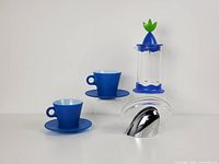 Two blue espresso cups with saucers, Guzzini napkin holder and Fiorello frother displayed on a white surface