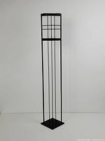 Front view of tall, slim metal and glass tealight holder against plain wall