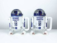 Pair of R2-D2 shaped plastic cups with handles, showing front view with lids on, standing upright