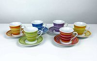 Full set of 6 espresso shot cups with corresponding saucers, each with a different colorful stripe pattern, displayed in a row.