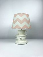 Full view of the table lamp showing the teacup base and pink and white chevron shade on a plain background.