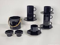 Photo showing six black octagonal cups stacked in pairs on matching octagonal saucers next to the black octagon ice bucket with handle - all glossy black glass.
