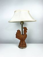 Front view of vintage ceramic rooster lamp with cream-colored double fabric shade, shown switched off against plain background.