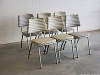 Group side angle view of 6 vintage chrome vinyl diner chairs in striped upholstery on a concrete floor against a white brick wall