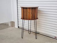 Front view of round wooden mini bar cabinet with closed tambour doors and metal hairpin legs