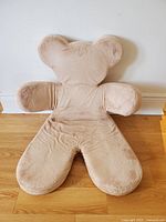 Front view of beige plush bear shaped child chair with head, arms, and legs visible