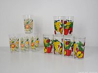 Two sets of vintage juice glasses displayed: A set of 4 glasses with assorted fruit design, and a set of 6 glasses with prominent grape and apple illustrations.