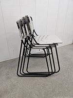 Side view of four stacked chairs showing black tubular frames