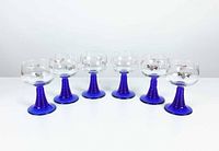 Front view of six roemer style glasses showing clear bowls and cobalt blue ribbed stems with grapevine decoration.