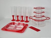 Full set showing all items: large and small red plastic fruit bowls with detachable handles, small red forks, red plastic condiment tray with four removable clear acrylic section trays, Bodum Oktett champagne flutes with red bases.