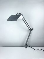 Front view of the silver-colored desk lamp extended upwards with clamp base and power cord visible.
