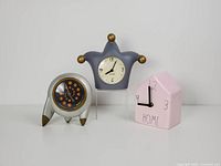 Lot of three vintage table clocks: jester-shaped gray clock, silver round clock with copper details, and pink ceramic house clock