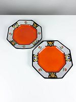 Two octagonal vintage plates with orange center and decorative floral black and white border laid side by side on white surface