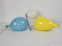 Three vintage ceramic wall decor balloons arranged side by side in white, light blue, and yellow. Butterfly cutout on blue balloon visible and blue ribbon on white balloon.