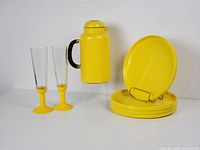Photo showing the Bodum yellow thermo jug with black handle, two yellow-based champagne flutes, and four yellow plastic plates stacked on a display