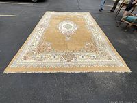 Full view of large rectangular wool area rug on asphalt, showing beige background and floral medallion pattern with decorative border.