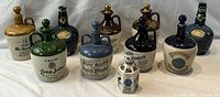 Photo showing all 10 vintage stoneware whiskey jugs arranged in two rows, with different colors and shapes including Glen Garry and Long John brands