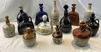 Front view of all 13 vintage Scotch whiskey decanters arranged in three rows showing variety of shapes, colors, and styles.