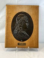 Full view of the bronze relief plaque featuring Marianne mounted on a wooden panel with brass plate at bottom center.