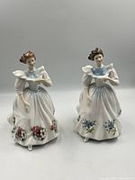 Two Royal Doulton figurines displayed side-by-side showing front view, highlighting floral skirt decoration.