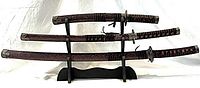 Three swords in scabbards on stand, angled view