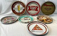 Seven round metal brewery advertising trays arranged in rows