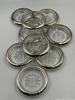 Photo showing all nine silver plated coasters stacked and spread out on a flat surface, revealing round glass inserts with starburst patterns and silver plated rims with beaded edges.