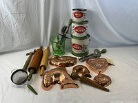 Entire collection including copper molds, honey tins, rolling pins, glass pitcher, strainer, meat tenderizer, and handheld beaters arranged on white background.