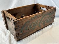 Left angled view of the antique Coca-Cola wooden crate showing the green painted logo and side handle cutout.