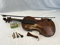 Full size antique Hopf violin with dark wood finish, included bow, tuning pegs, tailpiece, and small accessories laid out on white background.