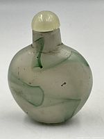 Front side view showing swirling green and white jade patterns and the rounded stopper on top.