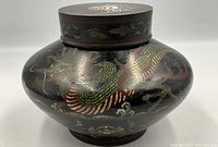 Side view of antique cloisonne jar showing dragon motif and dark enamel base.