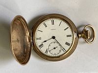 Watch open showing white enamel dial with black Roman numerals, subsidiary seconds at 6 o’clock and blued steel hands; full hunter front lid open.