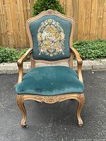 Front view of antique wooden arm chair with hand embroidered upholstery and velvet seat