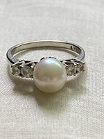 Front view showing round white pearl center with two diamonds on each side in prong settings