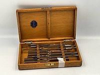 Open wooden box showing 10 medical tuning forks with metal forks, wooden handles, and cork spacers inside wooden compartments.