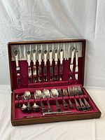 Complete flatware set in open wooden case with red velvet lining showing all pieces.