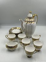 Full coffee service set displayed with coffee pot, sugar bowl, six cups, and seven saucers with ornate gold decorations on white porcelain.