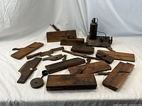 Collection of 16 antique wooden and metal tools arranged on white fabric backdrop with a small green apple for size reference