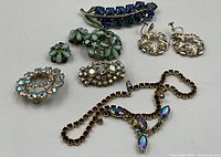Top view of the loose costume jewellery pieces including brooches, necklace, and earrings showing detail of rhinestones and metalwork.