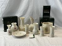 Front view of all 10 Irish porcelain items including vases, bowl, and planter pot with some in original black Belleek boxes.
