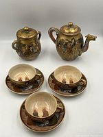 Oblique front view of teapot, sugar bowl, three cups and saucers