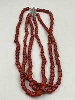 Three-strand red coral bead necklace laid flat showing bead arrangement and clasp
