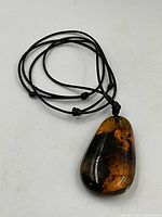Large amber pendant necklace with teardrop shaped pendant showing natural inclusions on a black cord with adjustable knots.