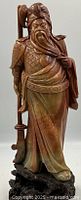 Full front view of the hand carved stone Chinese deity warrior with detailed armor and weapon, standing on rock-like carved base.