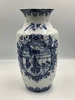 Front view of large white ceramic vase with blue Delft style painting showing a sailing ship framed by floral motifs.