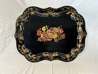 Top-down view of the entire black tole ware serving tray showing central floral decoration and scalloped edges with gold accents.