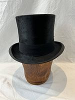 Black Lyons top hat shown on wooden head form against white background, front view