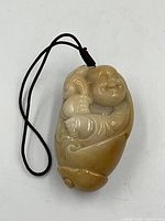Front view of the yellow jadeite carved Buddha pendant attached to a black cord.