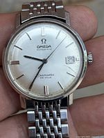 Close-up of watch dial showing Omega logo, hands, Seamaster De Ville text and date window.